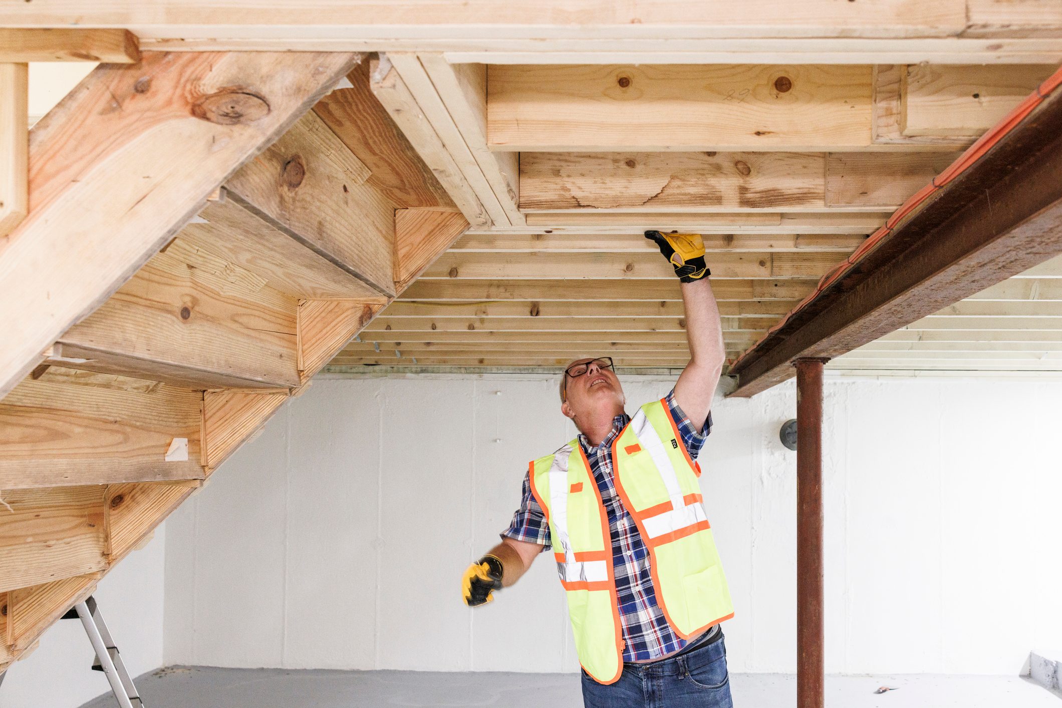 Inspection of wooden constructions in basement. Mature claim agent stand under wooden staircase in basement and check it