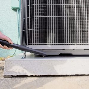 Home owner vacuums around heat pump to ensure peak efficiency for the HVAC system in Melbourne, Florida - USA