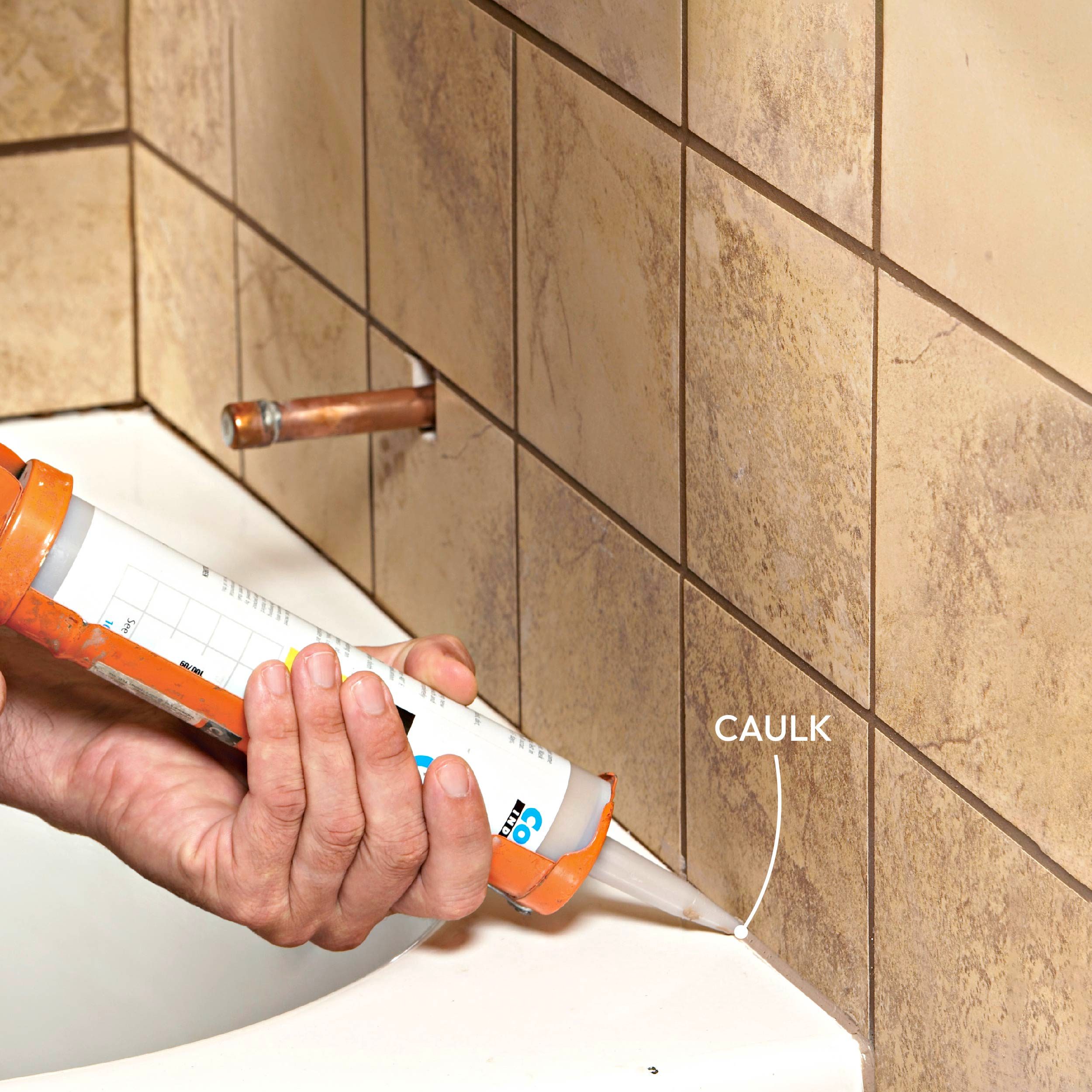 A hand is applying caulk between tiled surfaces near a bathtub, ensuring a waterproof seal along the joints.