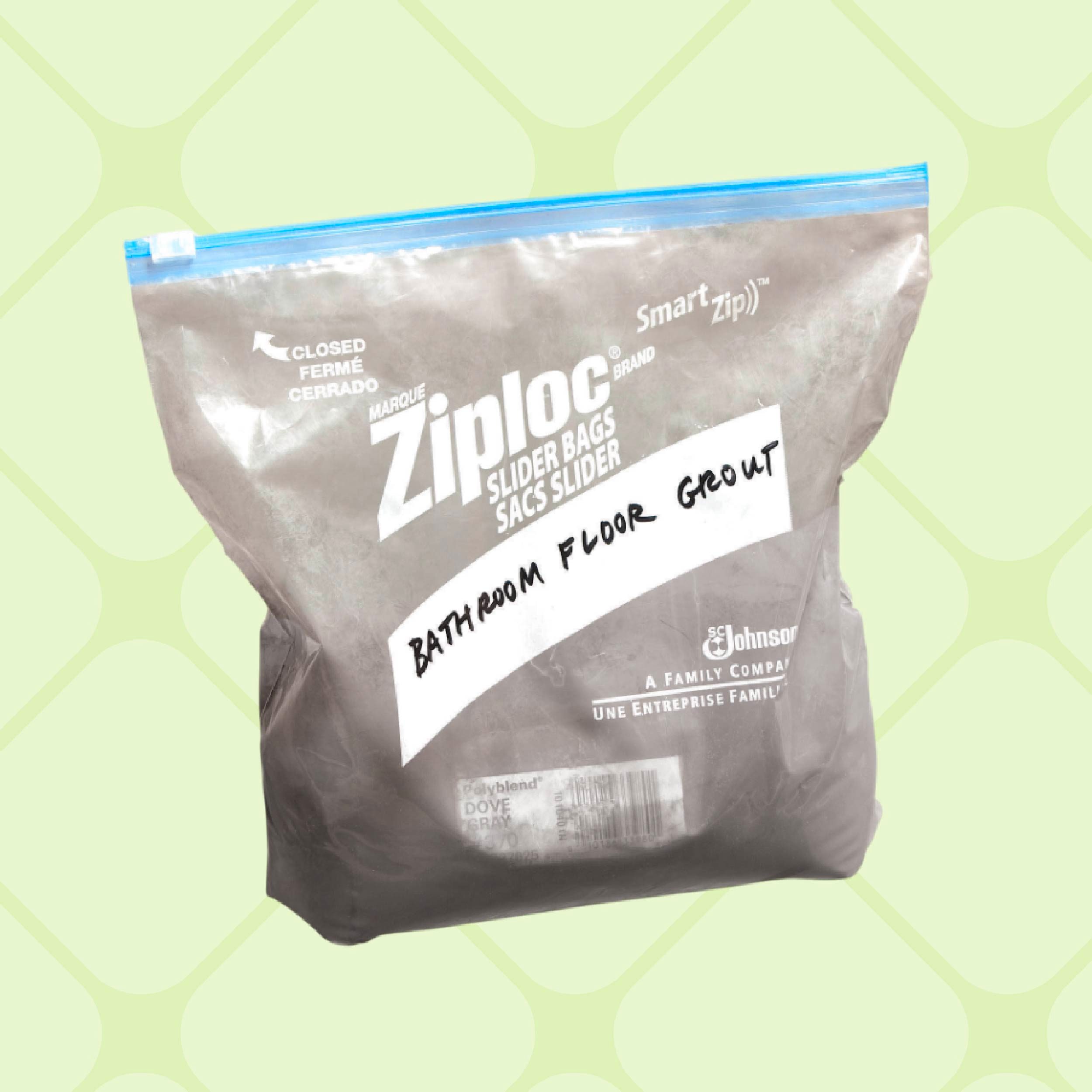 A transparent Ziplock bag labeled "BATHROOM FLOOR GROUT" contains gray powder, resting against a neutral background that emphasizes the bag's contents.