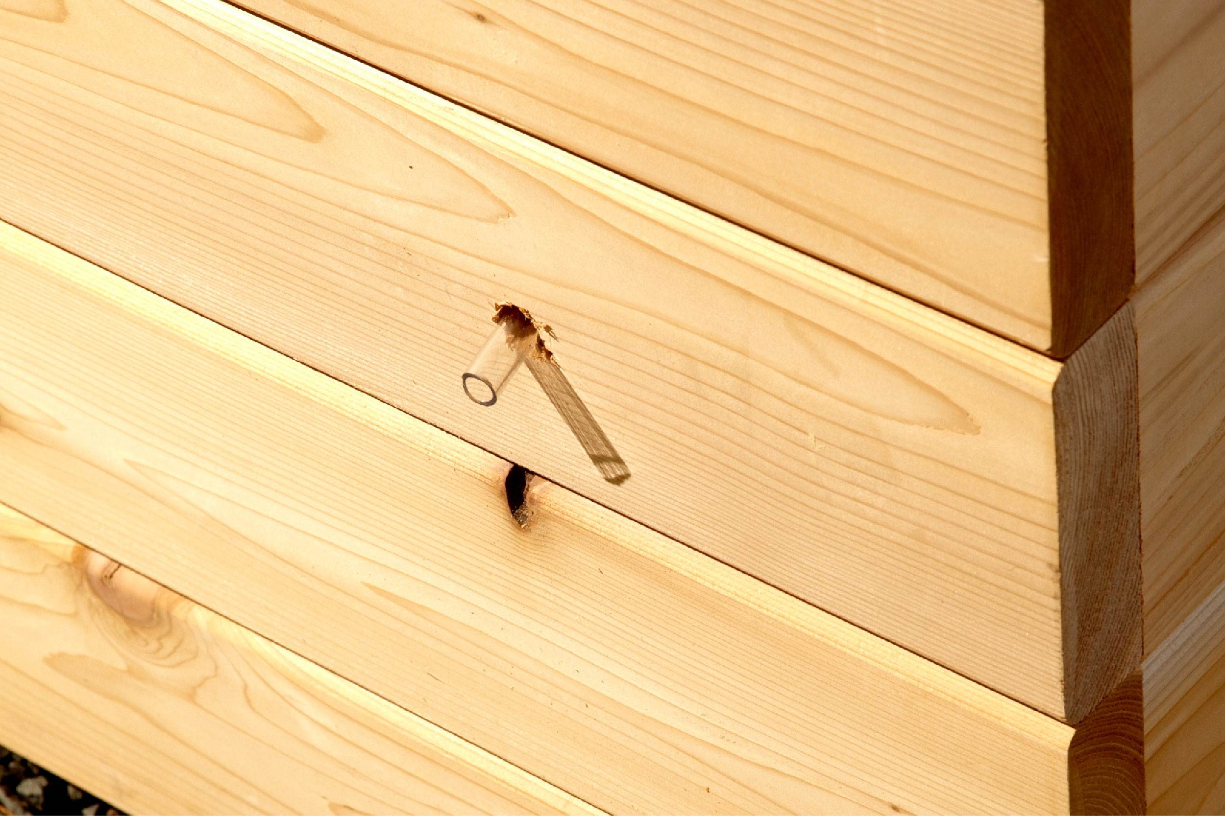 A wooden box features a small metal handle protruding from a hole, resting on a textured surface of gravel.