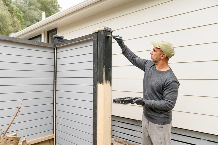 man staining fence outside house