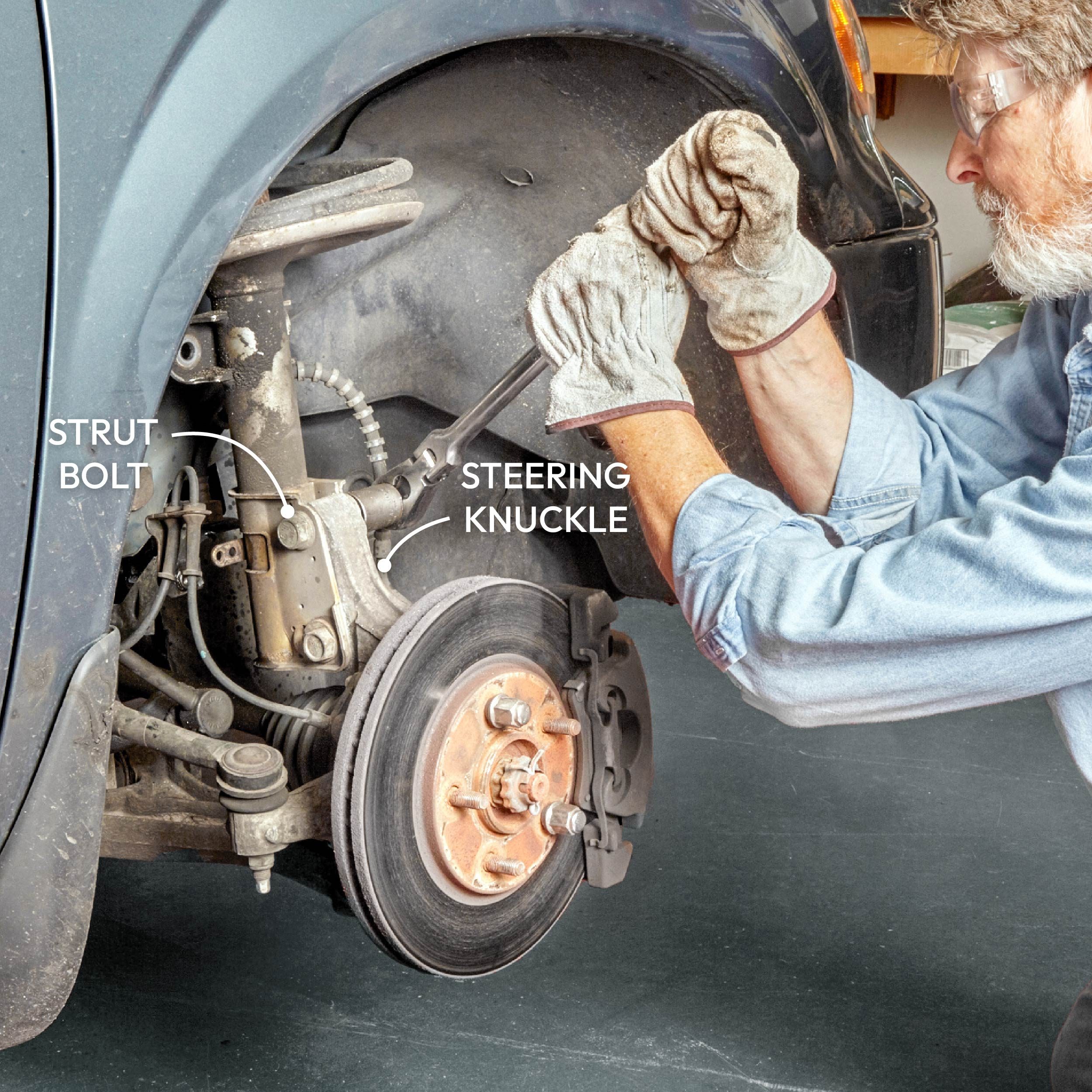 A person uses a wrench to tighten a bolt on a car's suspension system within a garage, with parts labeled for clarity.