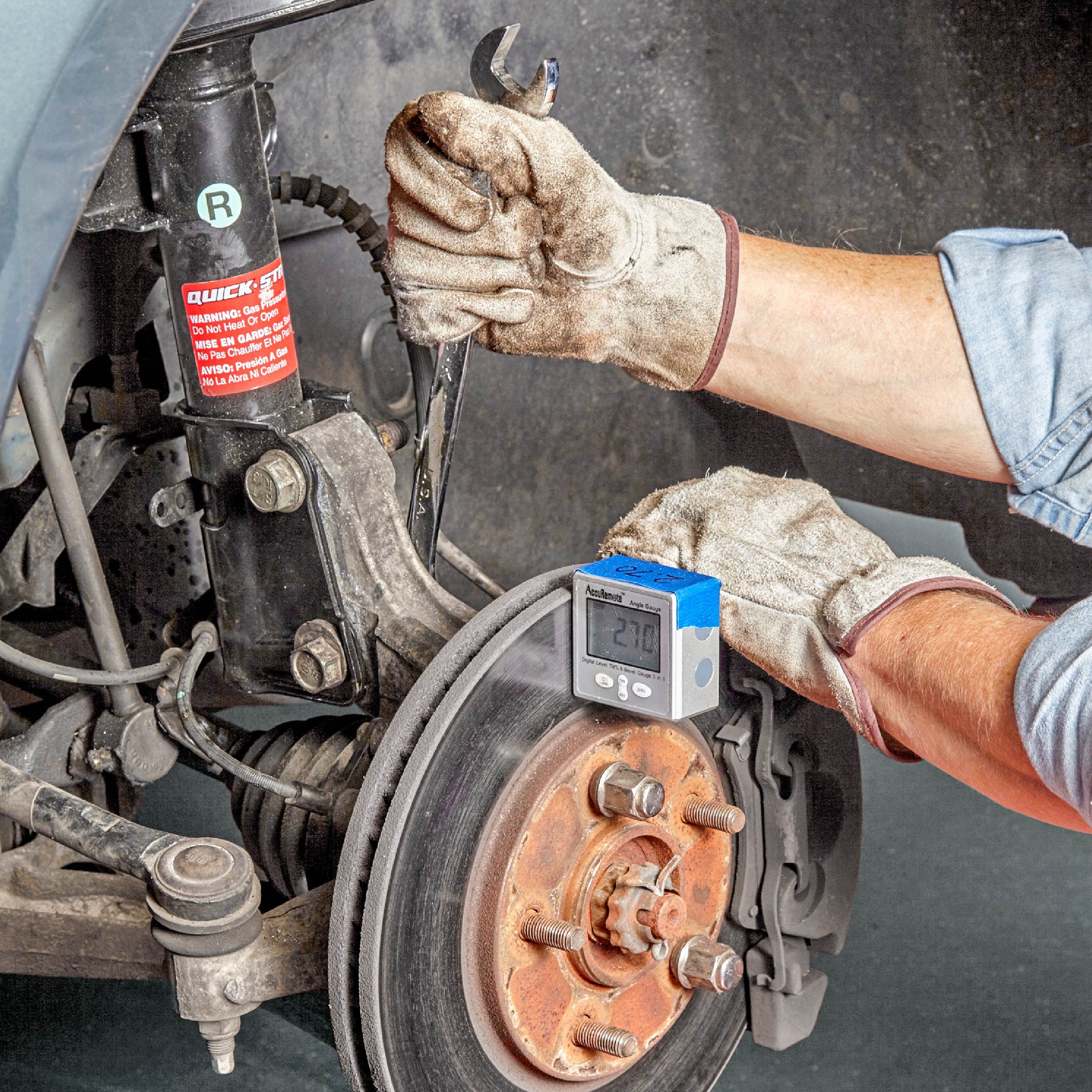 A hand holds a wrench, adjusting a car&rsquo;s brake assembly, while a digital gauge displays a measurement, all inside a vehicle workshop.