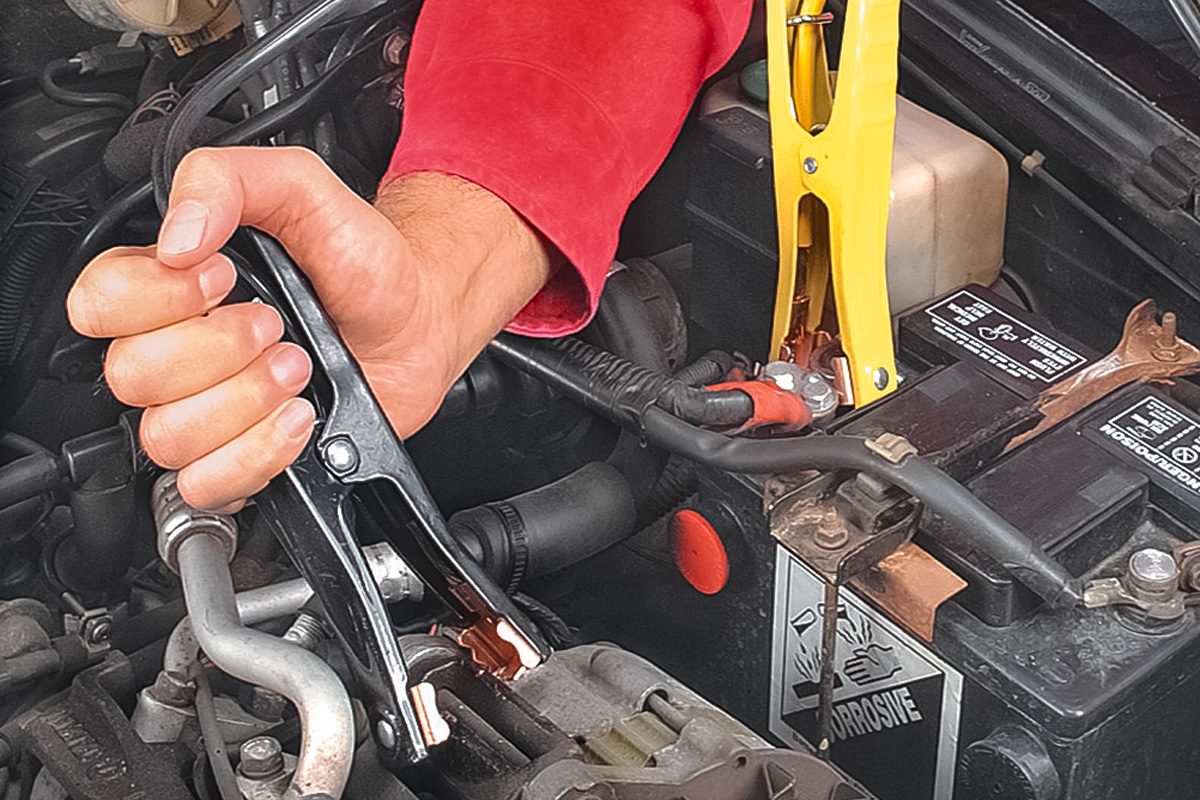 close up of hand connecting jumper cable to car battery