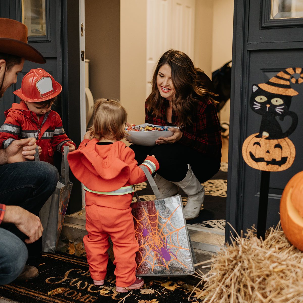A family dressed up for Halloween trick or treating, collecting sweets from a woman at her door.