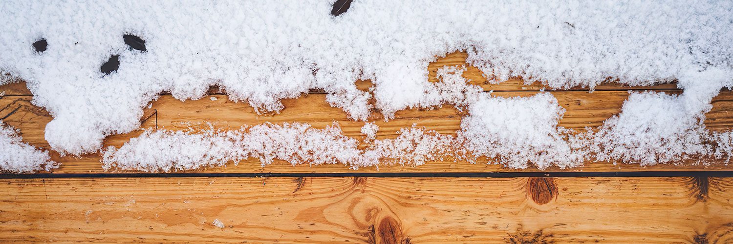 A Wooden Surface of a deck with snow on the top edge of the frame