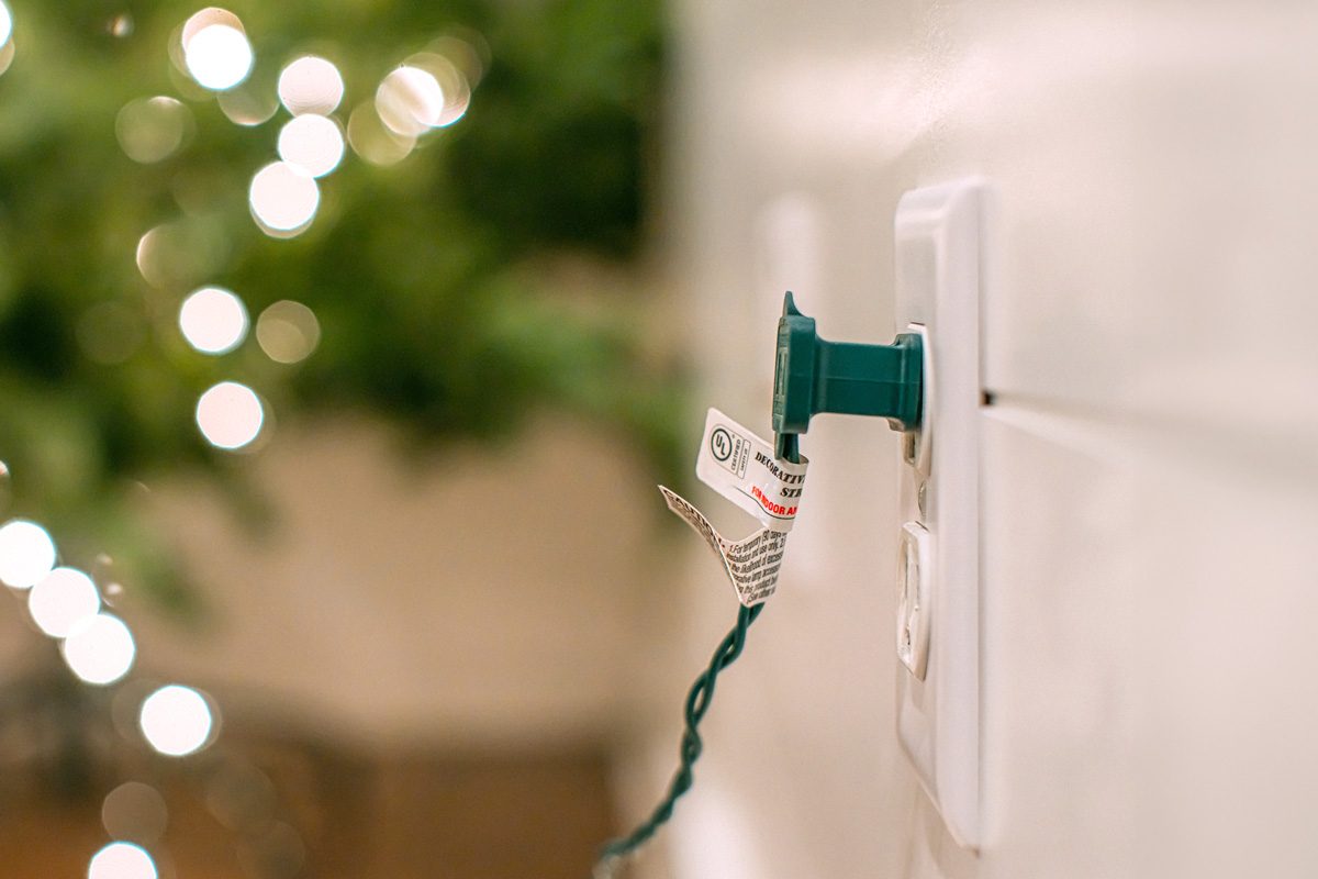 Electrical Connector Plugged into a Wall Outlet powering Christmas Lights Decorating a Tree