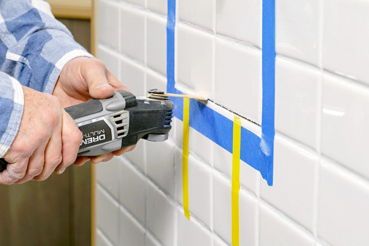 close up of hands using multi tool to cut an opening for shower valve replacement