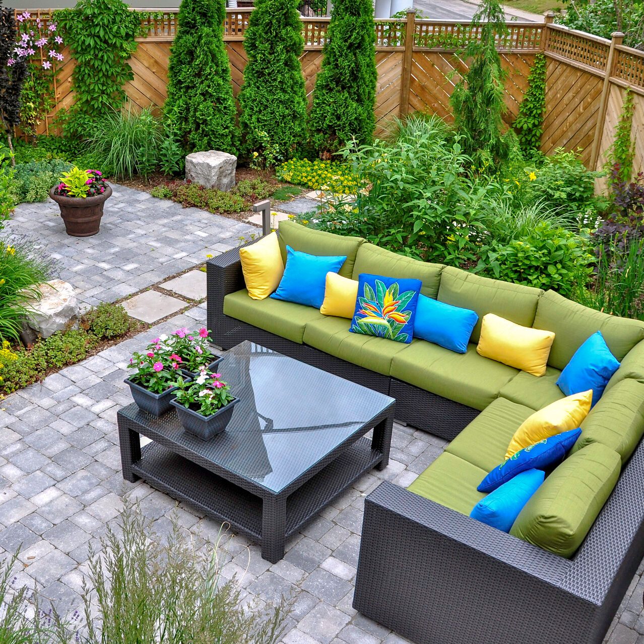 A beautiful small, urban backyard garden featuring a tumbled paver patio, flagstone stepping stones, and a variety of trees, shrubs and perennials add colour and year round interest.