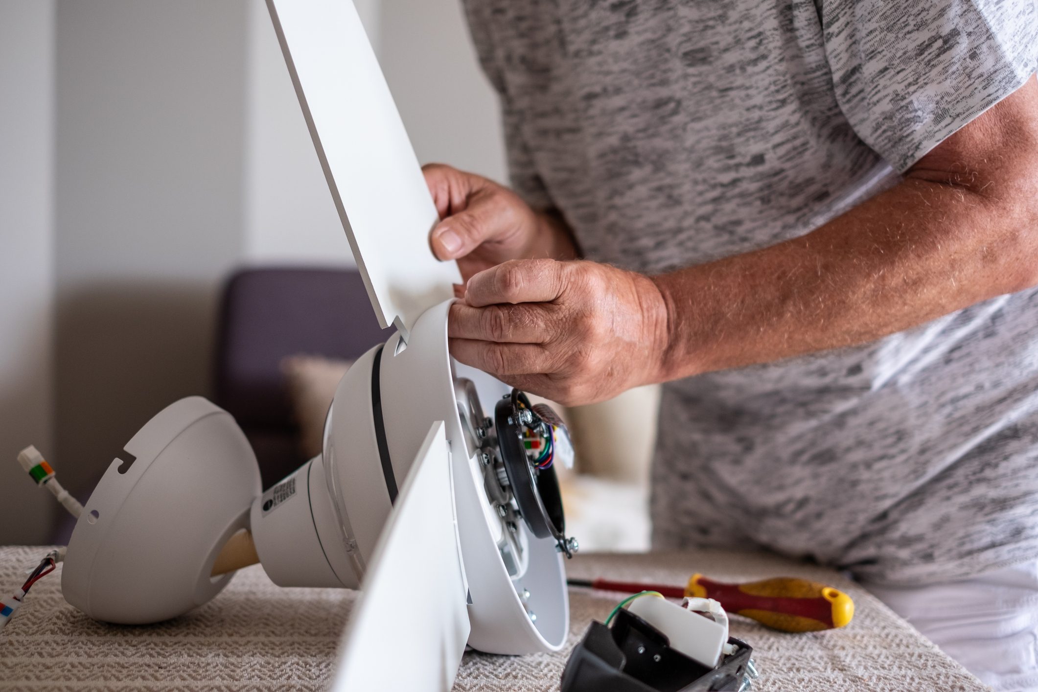 Senior man works installing a paddle fan on the ceiling at home, home improvement and DIY concept