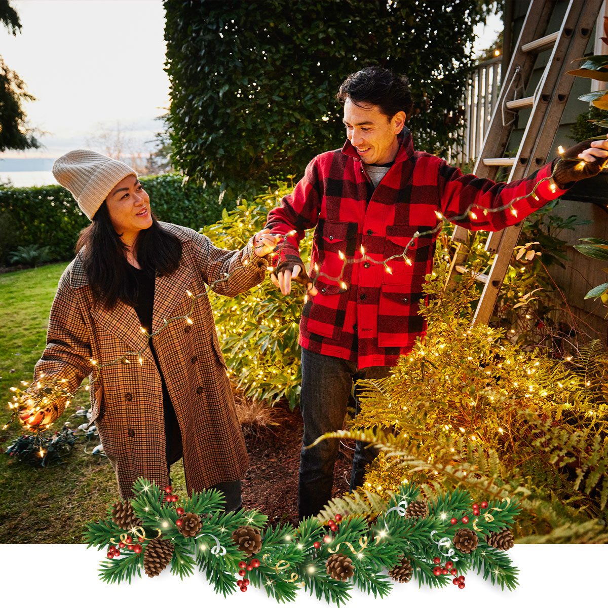 Medium wide shot of smiling couple decorating exterior of home with Christmas lights on winter evening