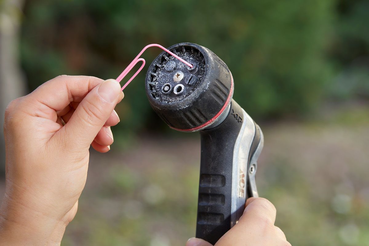 hand using a paper clip to unclog a spray nozzle on a hose outdoors