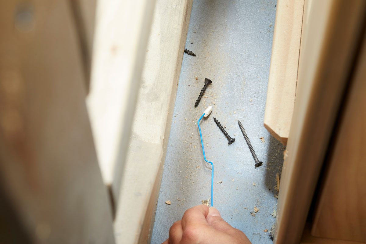 Hand using unwrapped paper clip with a dab of putty on the end to retrieve drop screws in a tight, hard to reach space