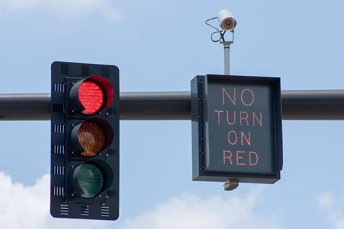 Red traffic light with "No Turn On Red" sign and intersection camera.