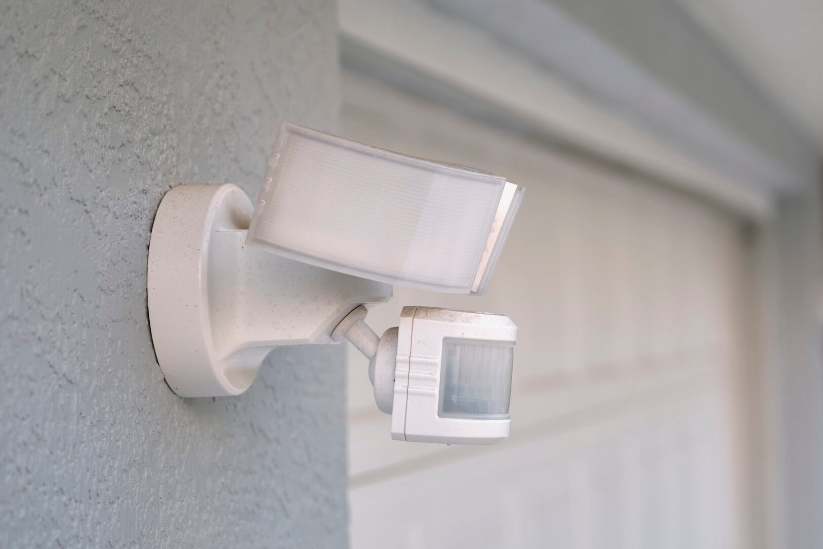 Motion sensor with light detector mounted on exterior wall of private house as part of security system