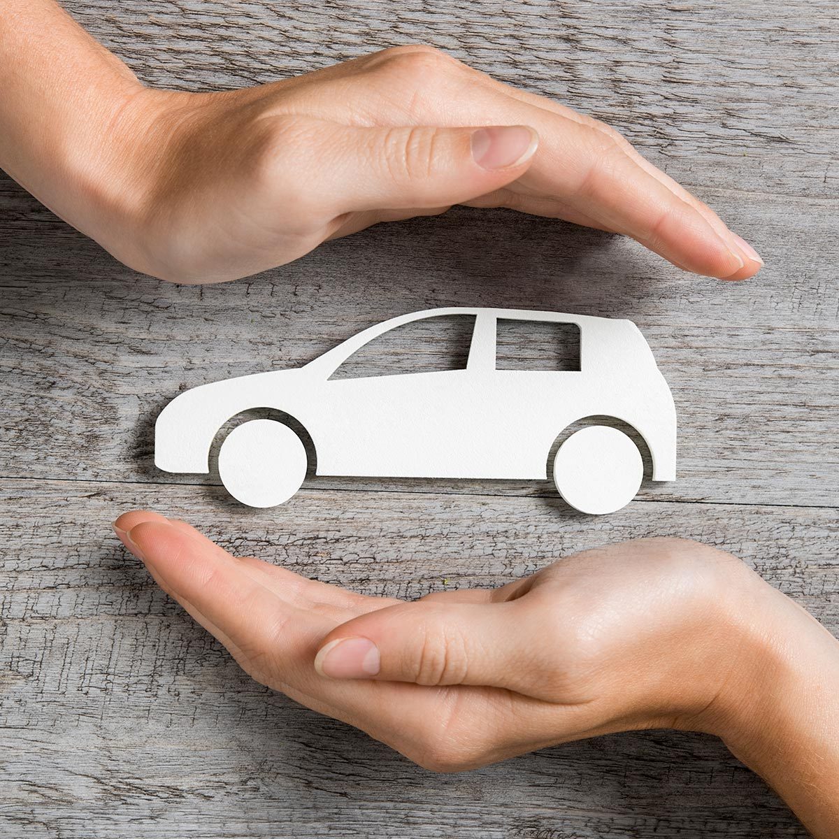 Hands protecting icon of car over wooden table. Top view of hands showing gesture of protecting car.