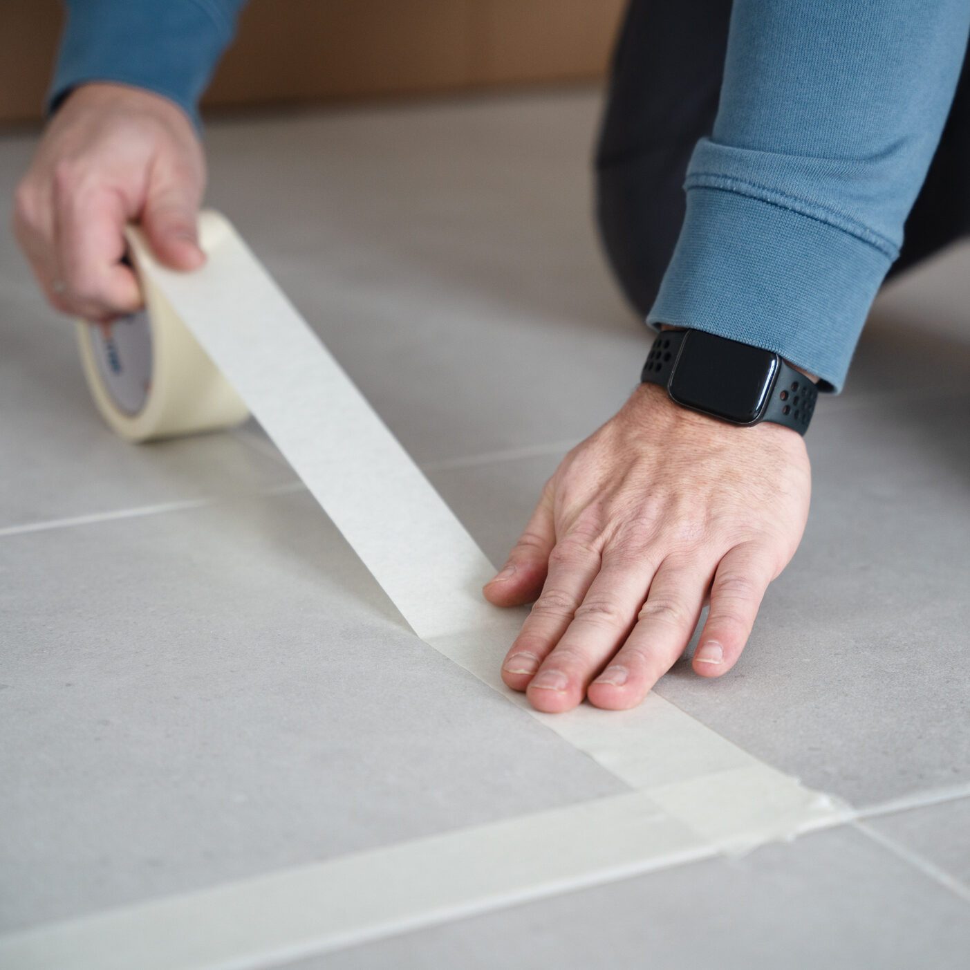 A man uses masking tape on tiled floor, planning markings for furniture
