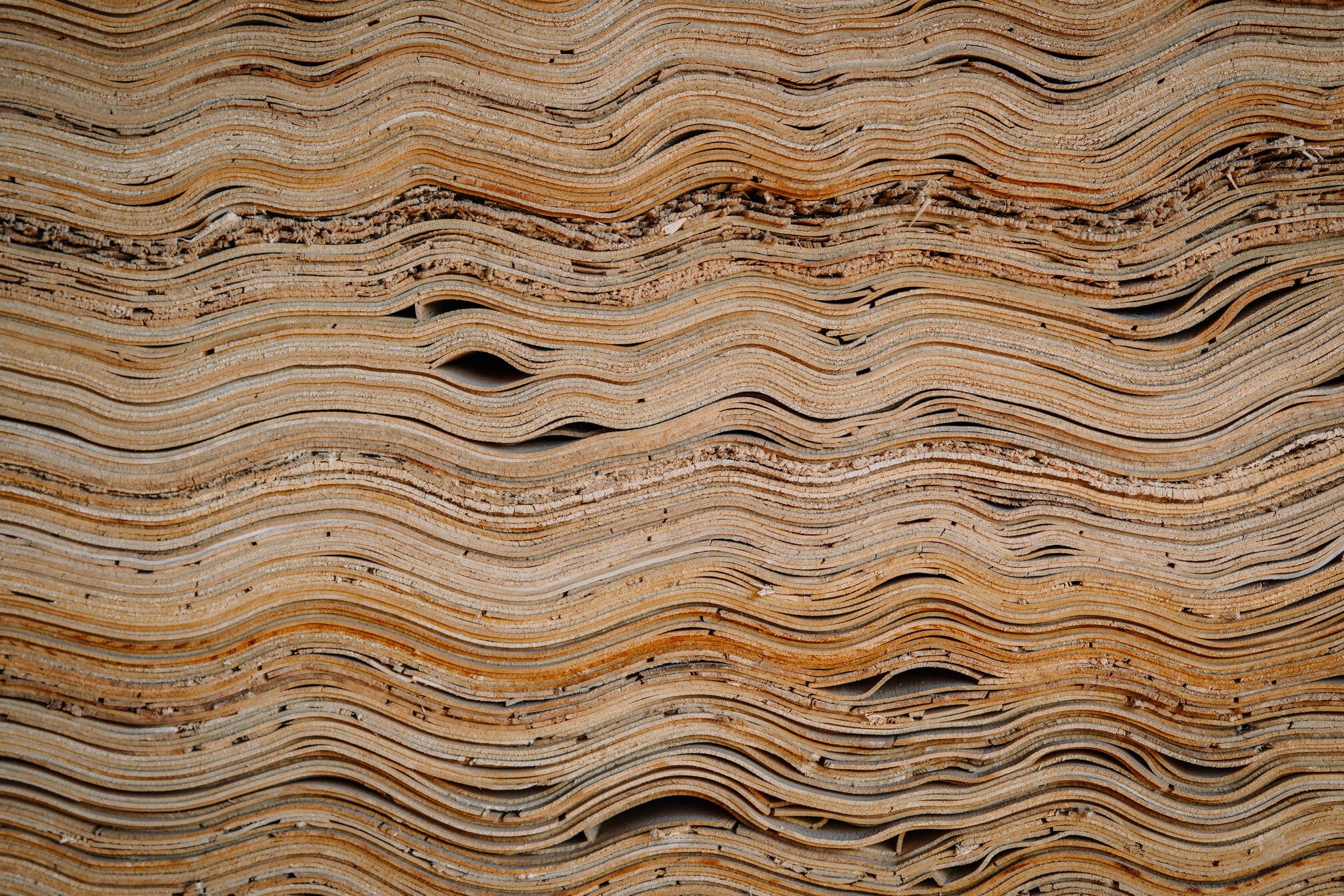 Close-up of stacked veneer wood sheets with natural wavy textures and organic lines, showing intricate patterns and fine grain in a woodworking setting.
