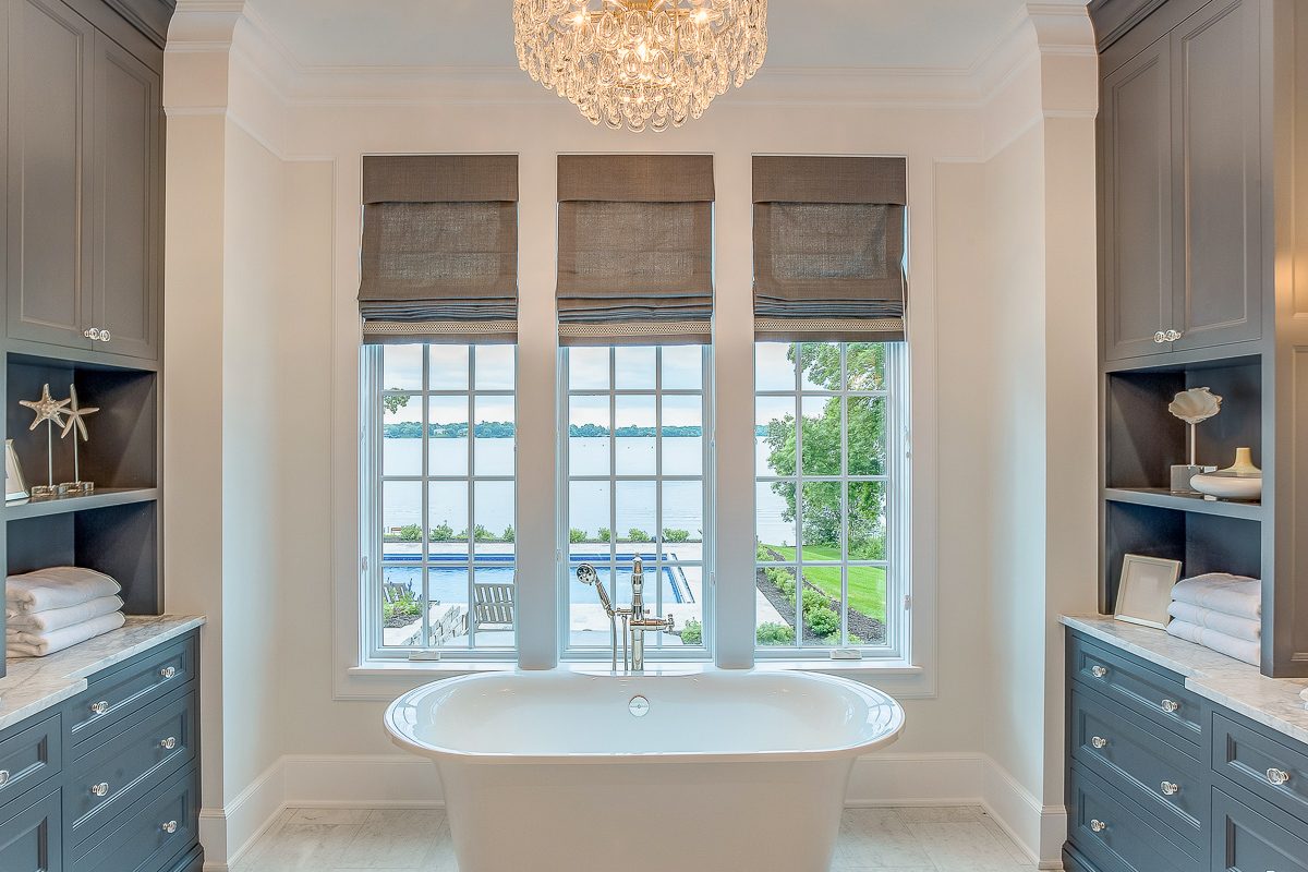 tall windows with shades behind bathtub